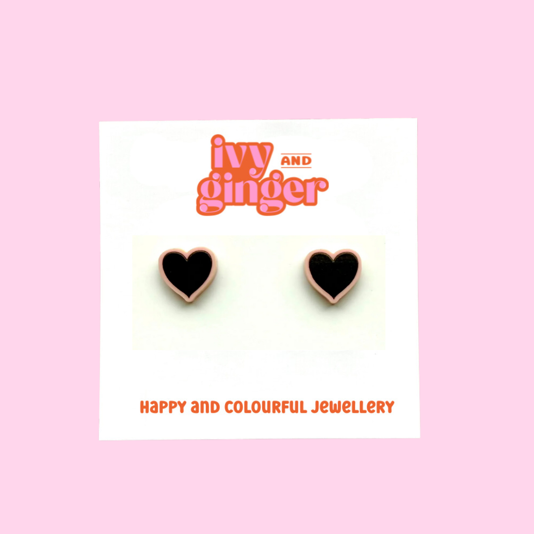 A pair of pastel pink heart shaped acrylic earrings with a bold black heart. The earrings are displayed on a white backing card with the brand name 'ivy and ginger'.