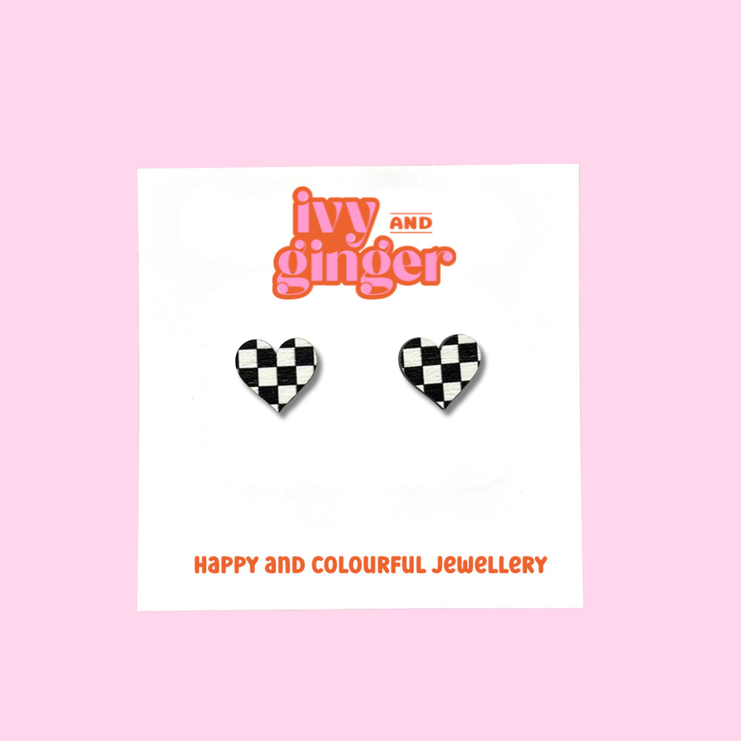 A pair of heart shaped earrings with a black and white checkerboard pattern. The earrings are displayed on a white backing card with the brand name 'ivy and ginger' at the top.