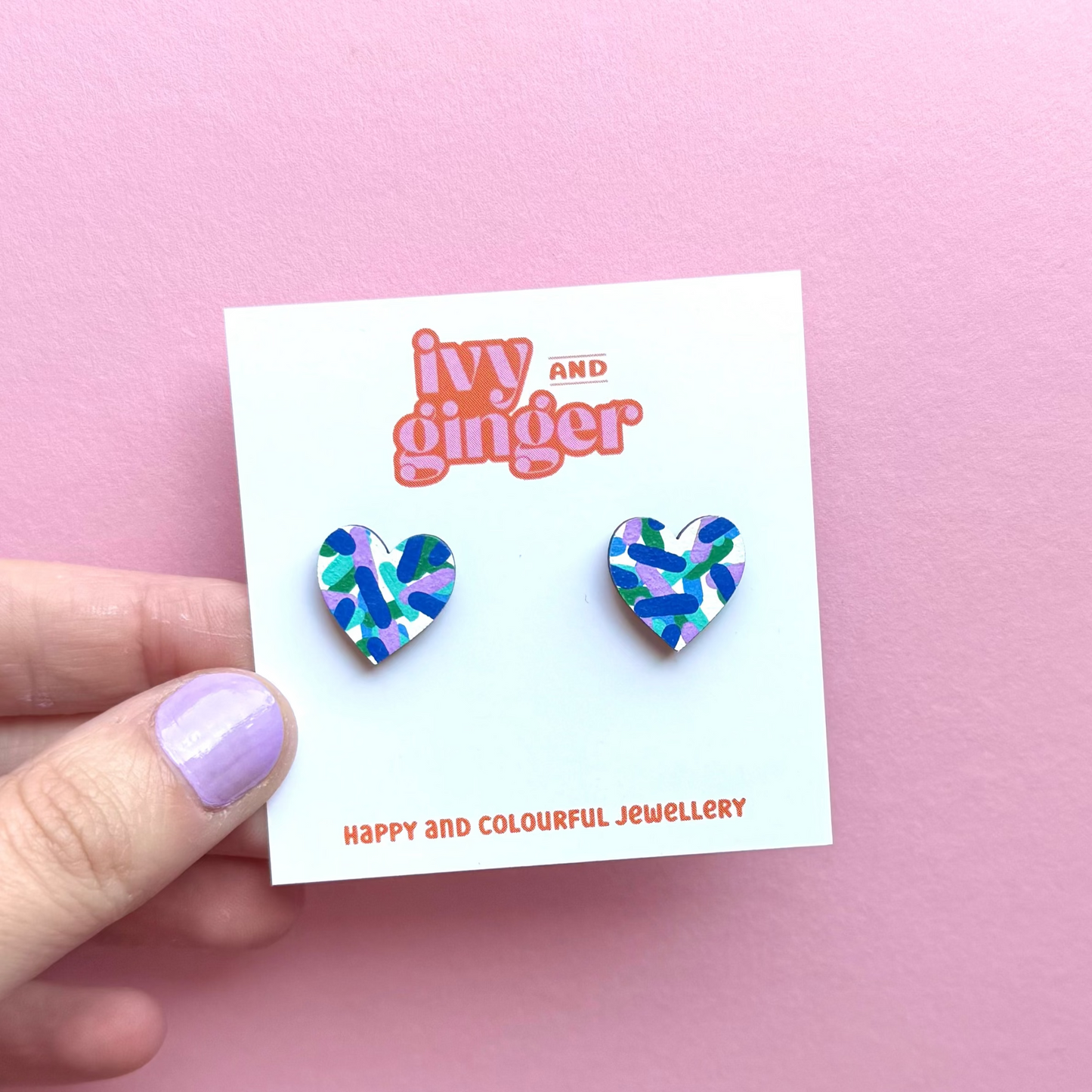Heart-shaped earrings on a 'Ivy and Ginger' branded card against a pink background