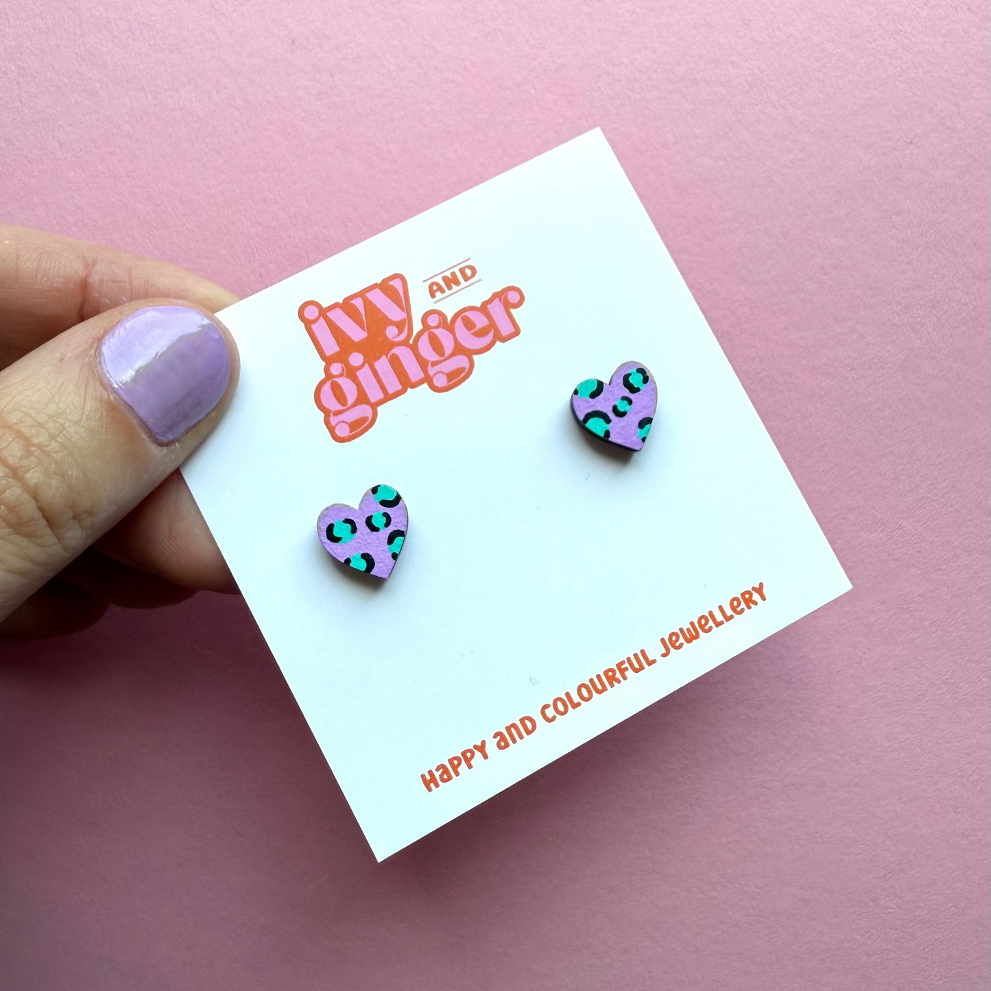 Heart-shaped earrings on a 'ivy and ginger' branded card against a pink background