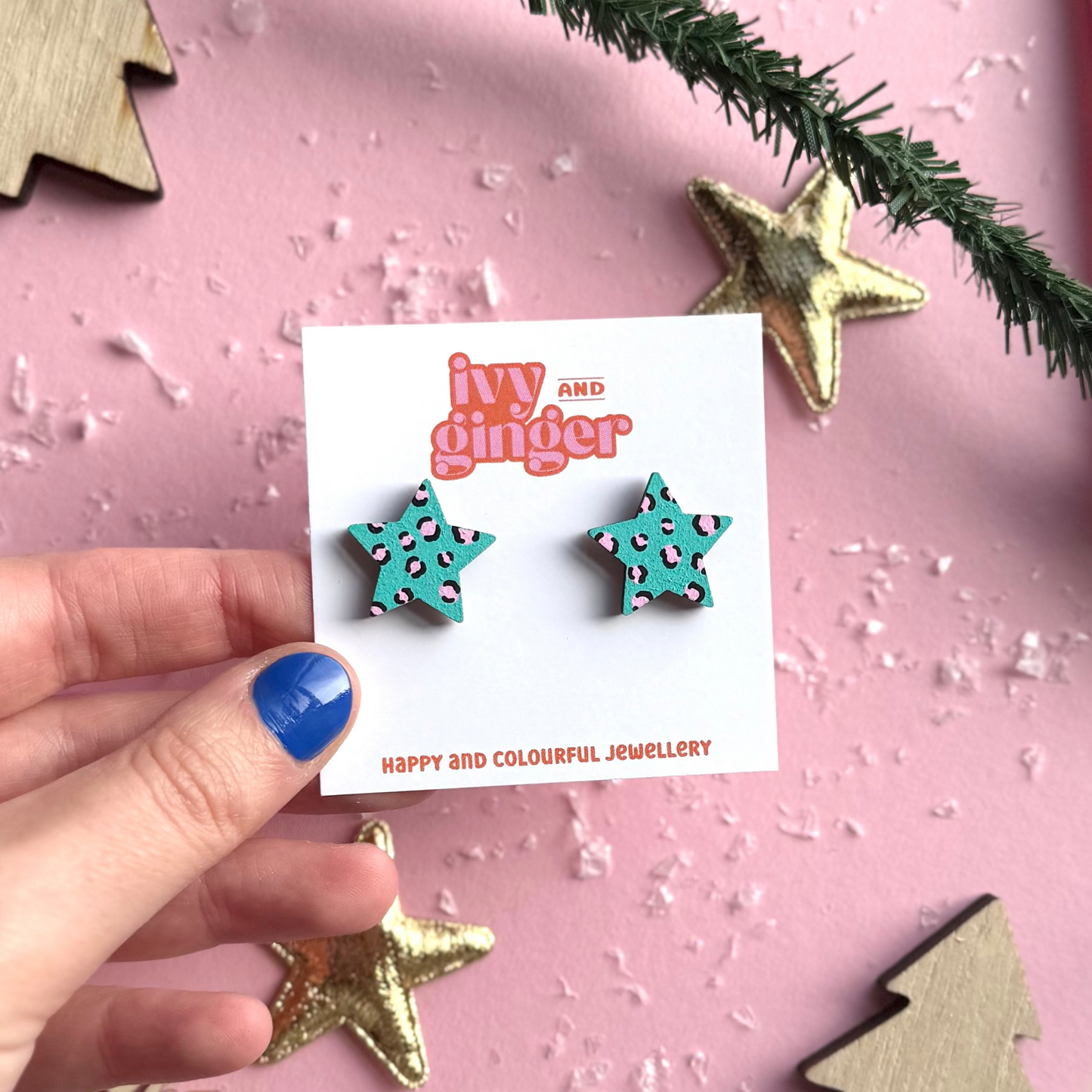 Star-shaped earrings held by a hand with a pink background and decorative elements.