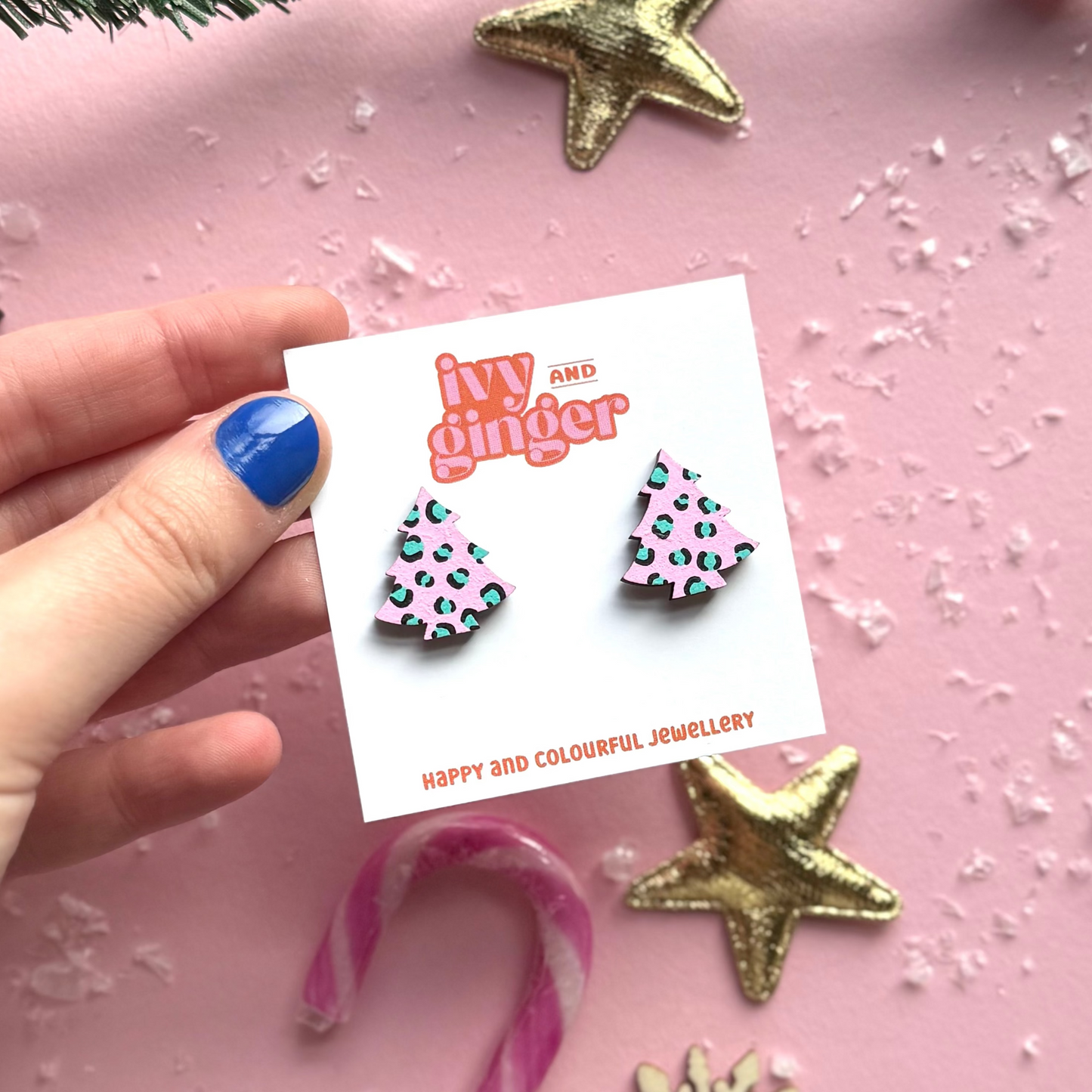 Hand holding a card with earrings and decorative Christmas items on a pink background