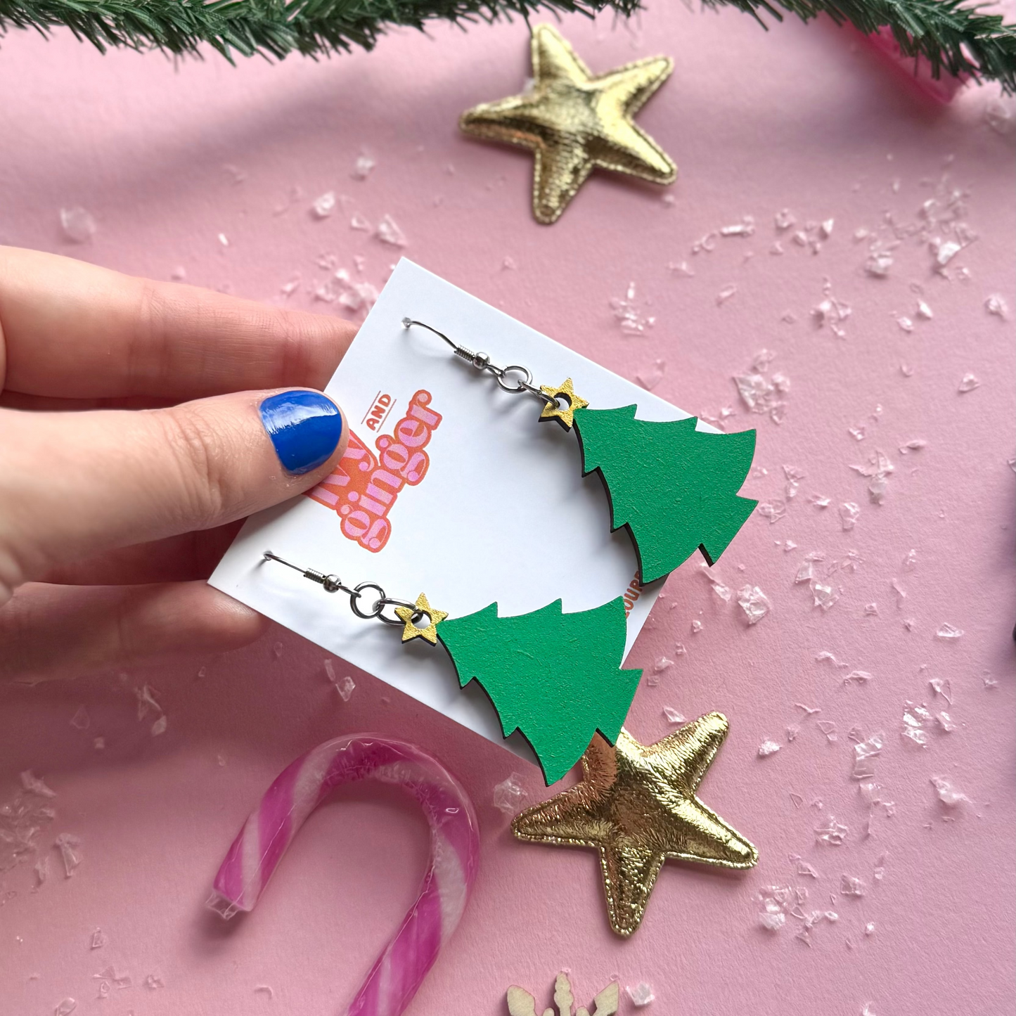Hand holding Christmas-themed earrings with a pink background