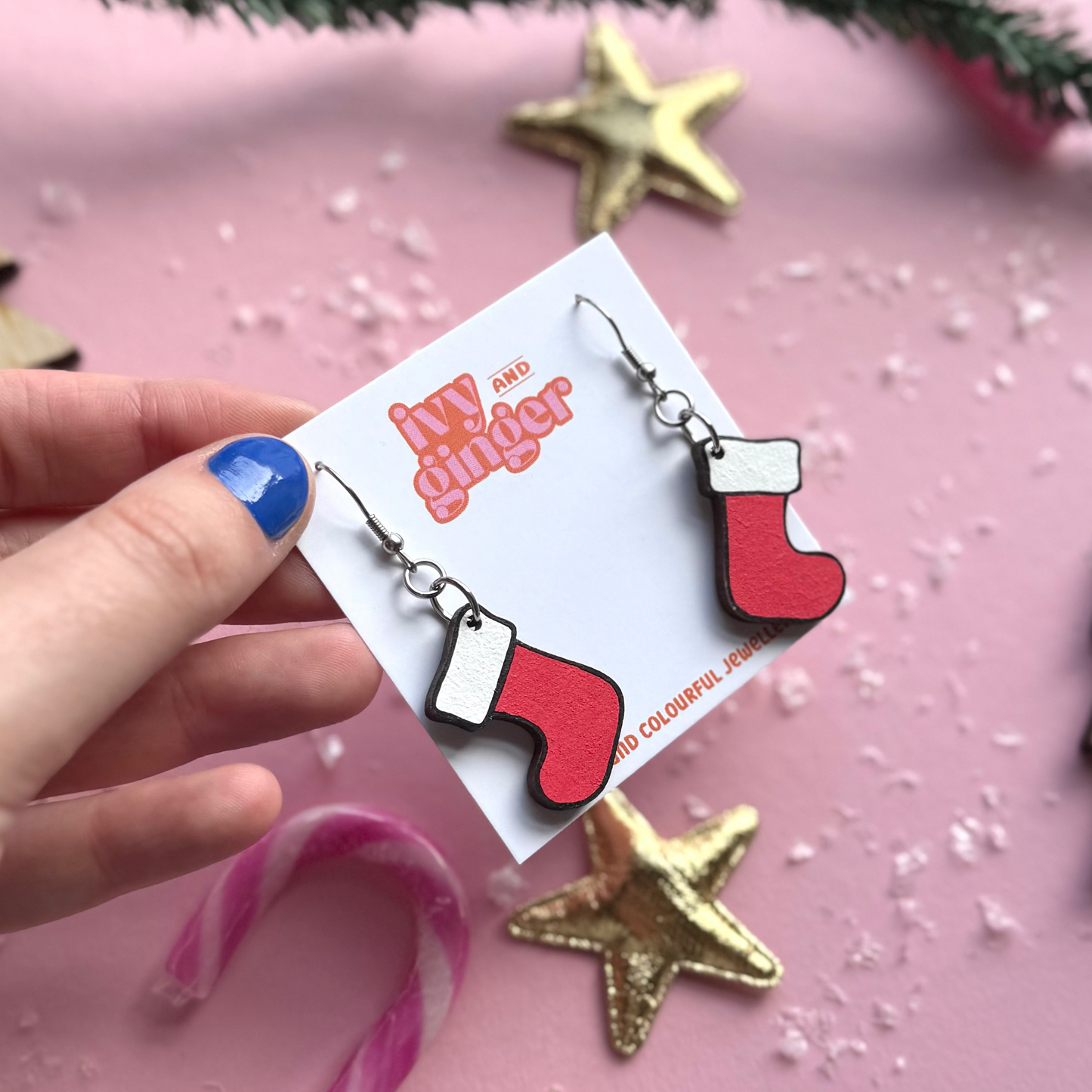 Hand holding Christmas-themed earrings on a branded card with festive background