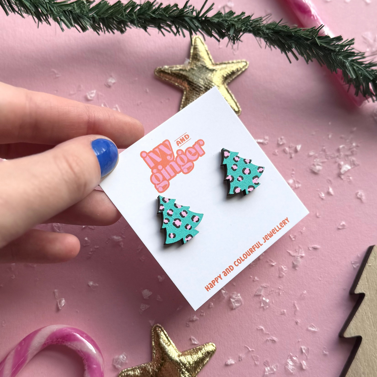 Tree-shaped earrings on a branded card with Christmas decorations on a pink background