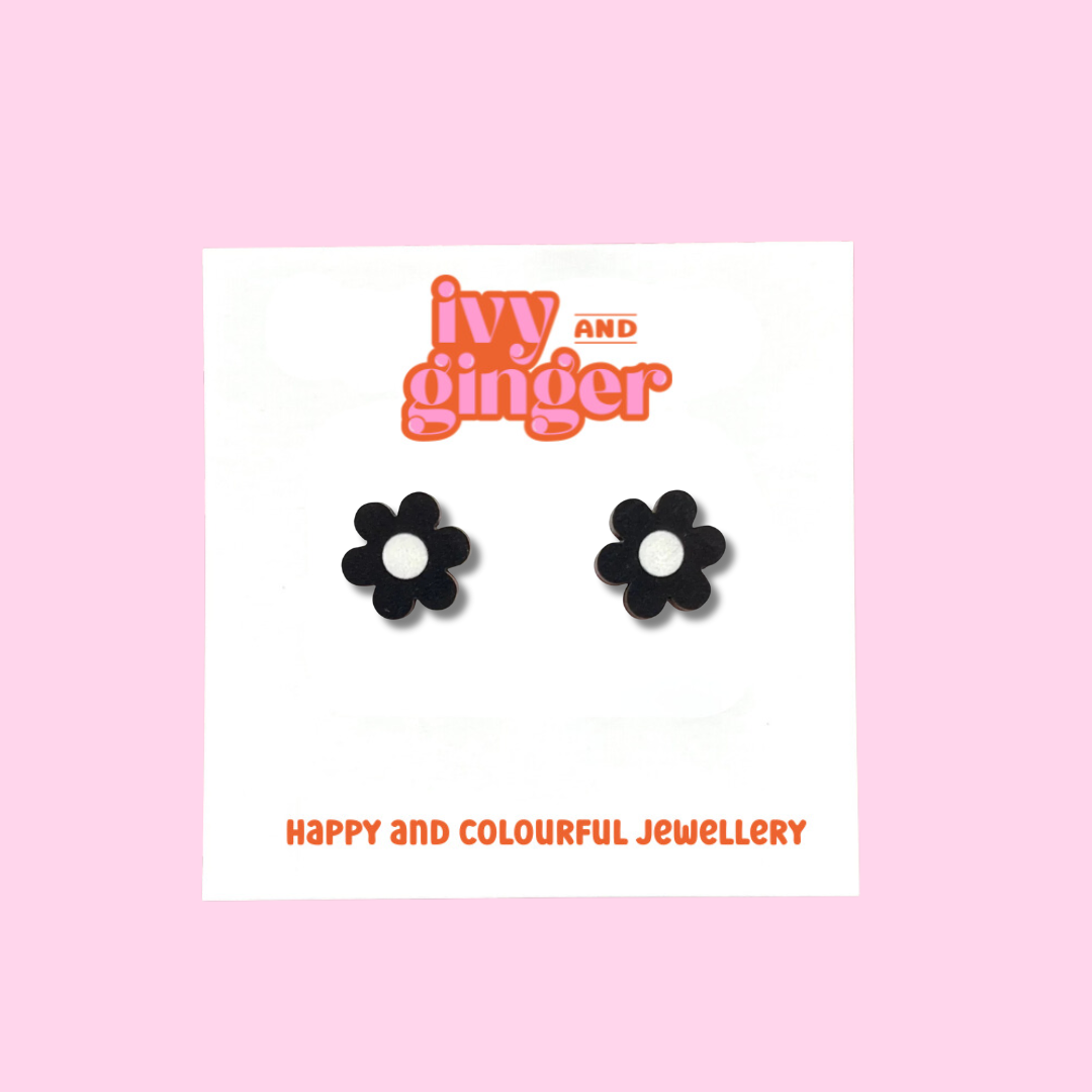 A pair of black daisy shaped wooden earrings with a white circle in the centre. The earrings are displayed on a white backing card with the brand 'ivy and ginger' at the top.