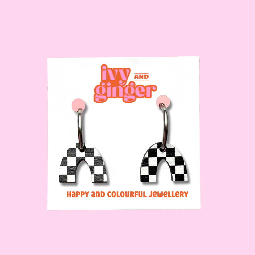 A photograph and arch shaped earrings with a black and white checkerboard print attached to steel hoops, presented on a white backing card with the brand name 'ivy and ginger'.