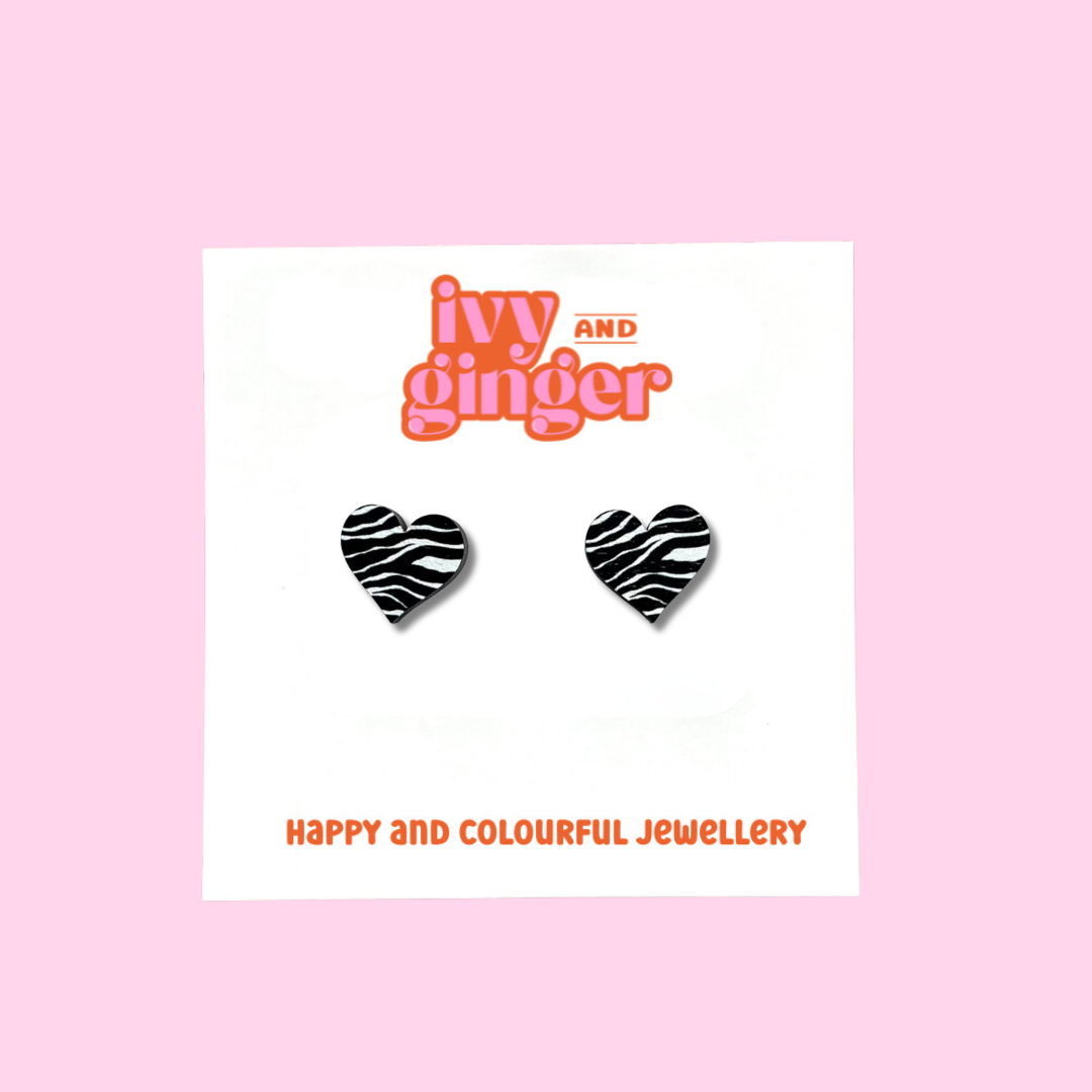 A pair of heart shaped studs with a black and white zebra print. The studs are displayed on a white backing card with the brand name 'ivy and ginger' at the top.