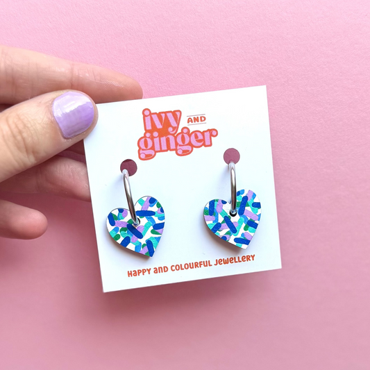 Heart-shaped earrings on a 'ivy and ginger' branded card against a pink background