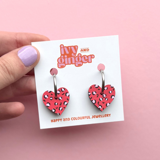 Heart-shaped earrings on a 'Ivy and Ginger' branded card against a pink background