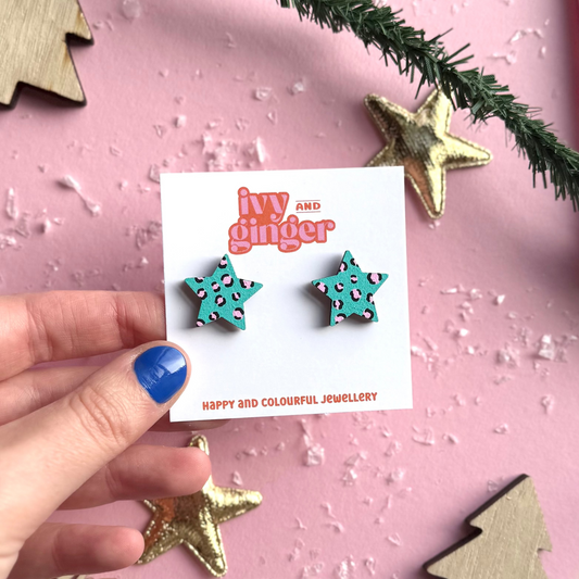 Star-shaped earrings held by a hand with a pink background and decorative elements.